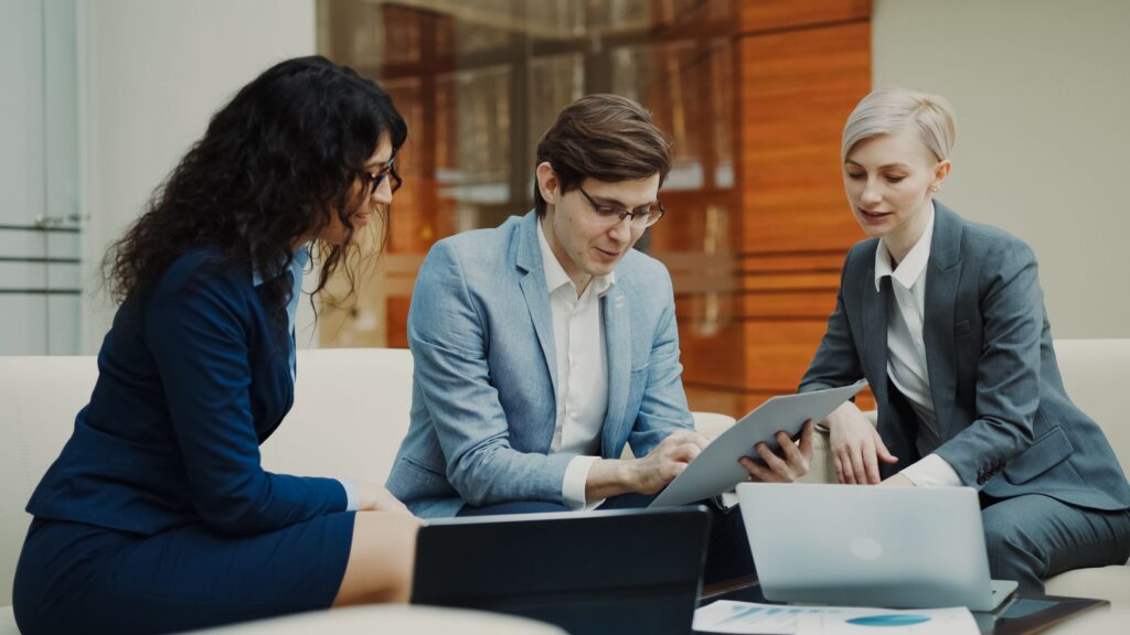 Three professionals engaged in a collaborative business meeting, using digital devices indoors.
